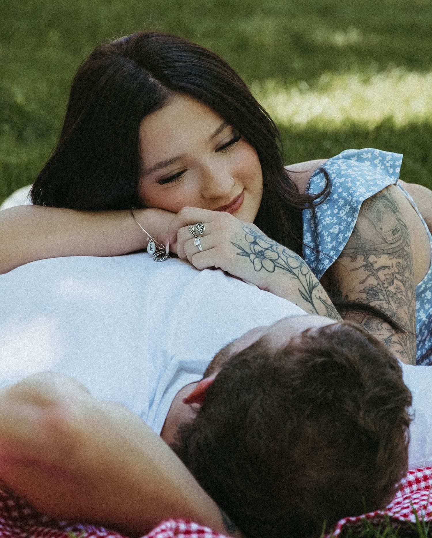 Two people sharing a romantic moment while lying together on a picnic blanket in the grass.