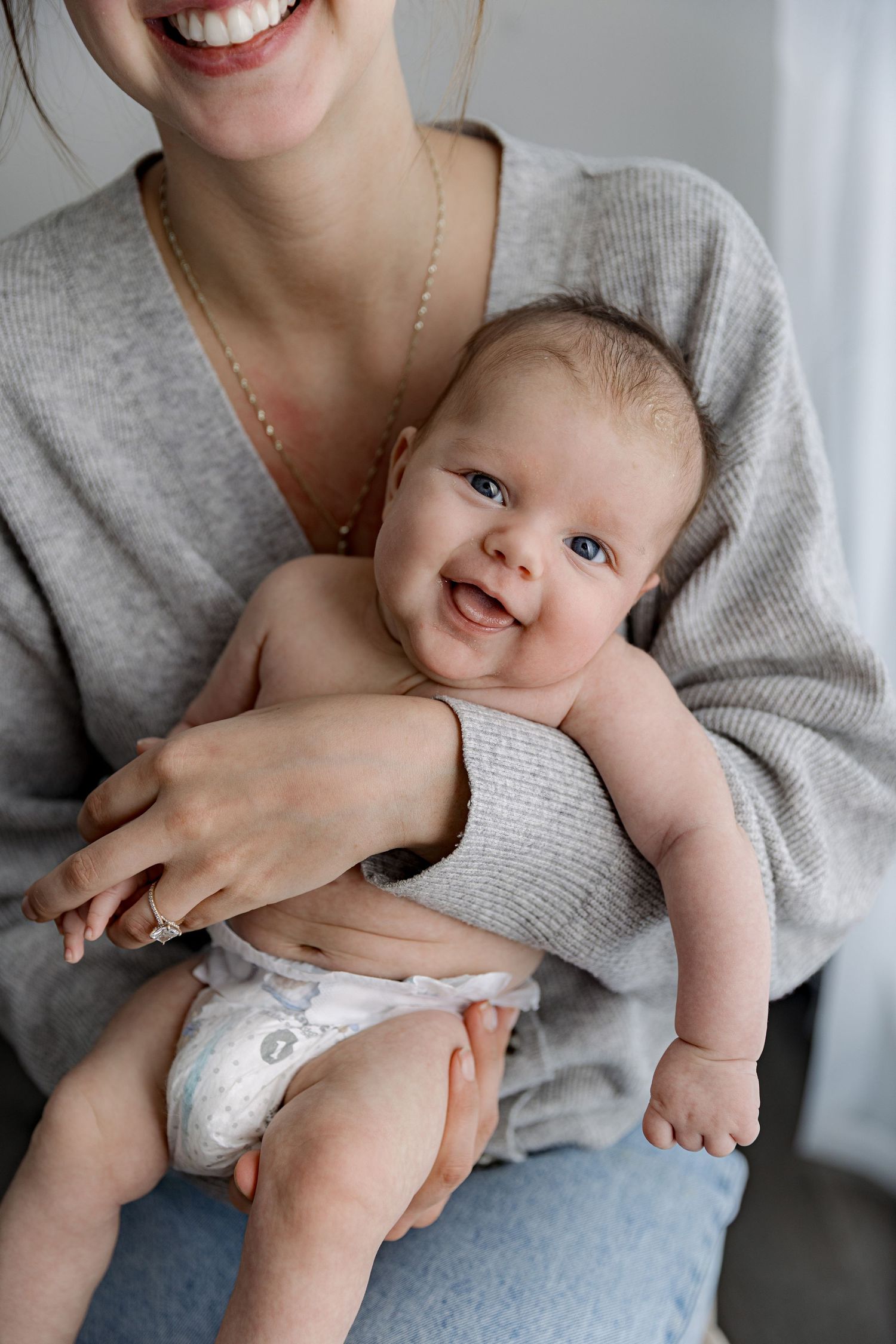 A series of five photos showing a baby in a white onesie being held and smiling while wearing a grey sweater.