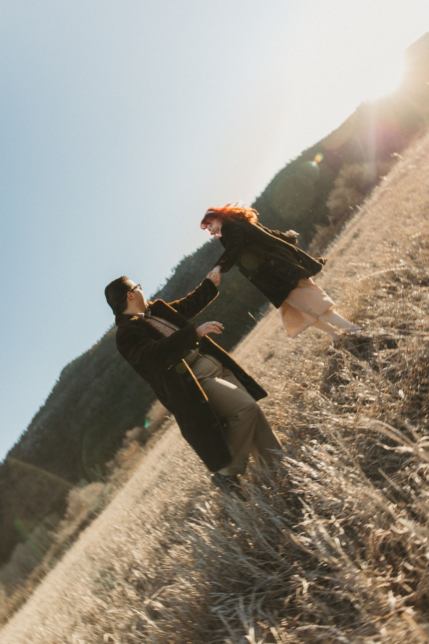 A person in dark clothing falls backwards onto a grassy hillside during sunset, creating a dynamic action sequence.
