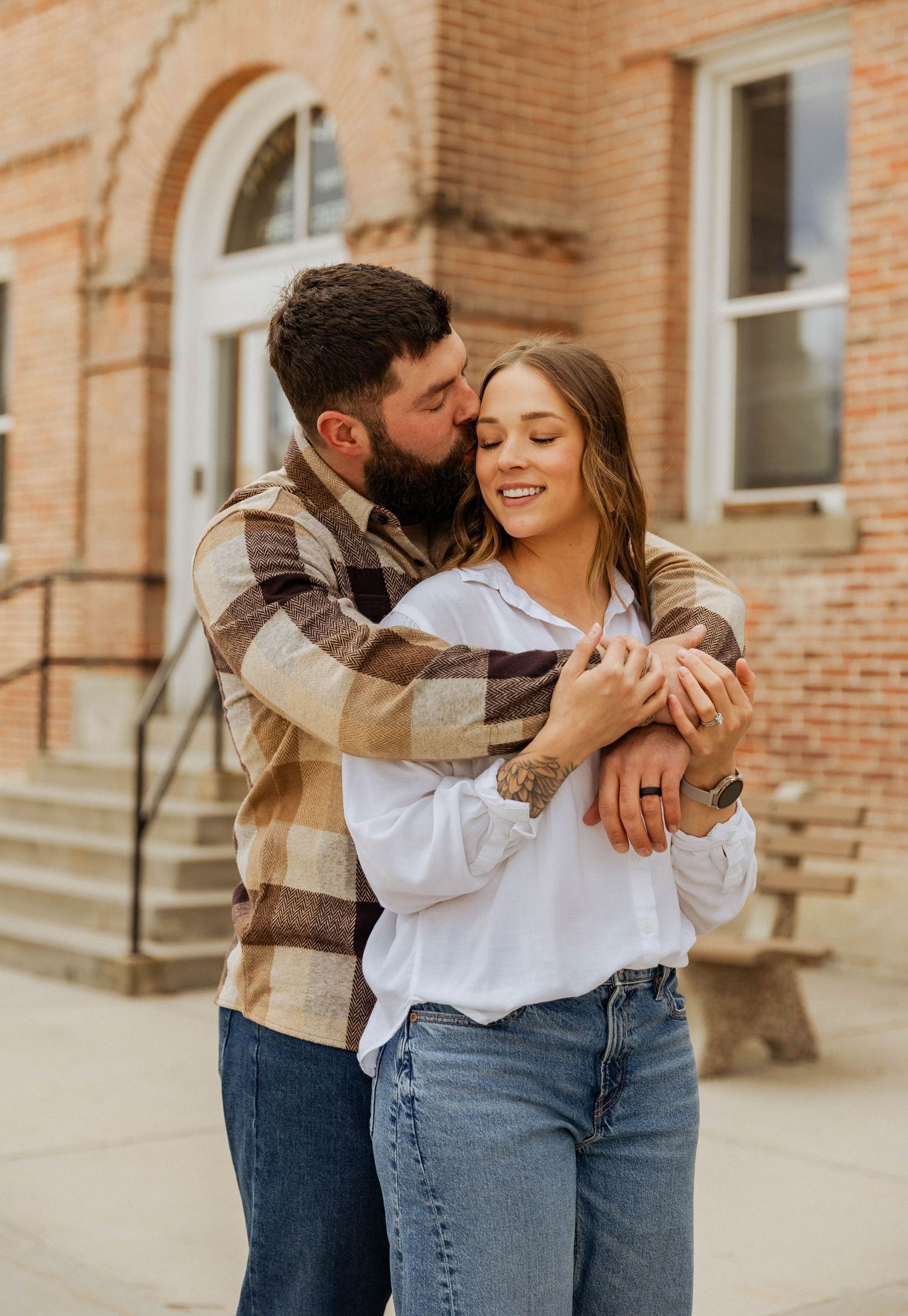 A tender moment between a couple in casual clothing hugging outside a brick building.