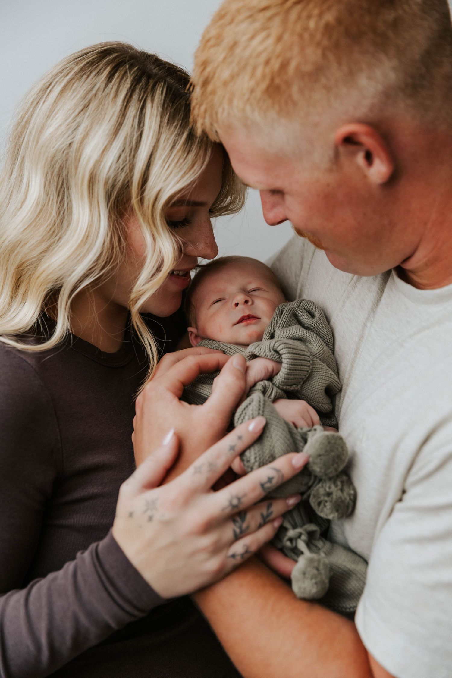 Parents sharing tender moments with their sleeping newborn baby in a series of intimate black and white photographs.