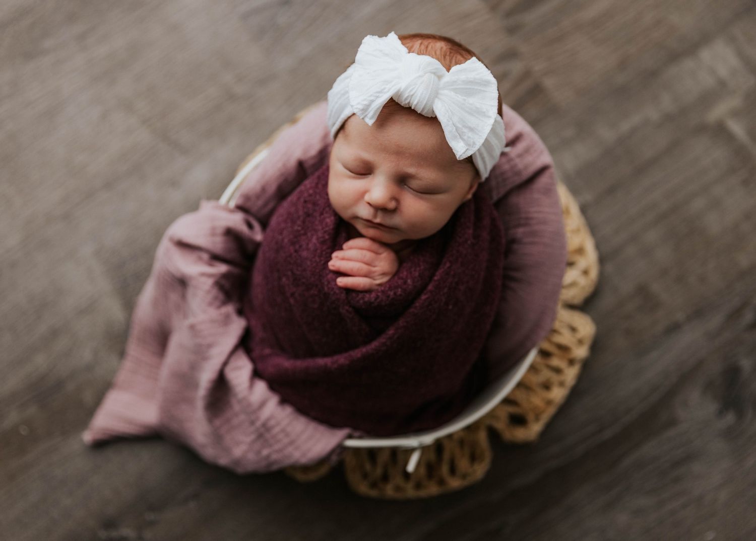Sleeping baby wrapped in burgundy and pink swaddles photographed from different angles with soft mood lighting.