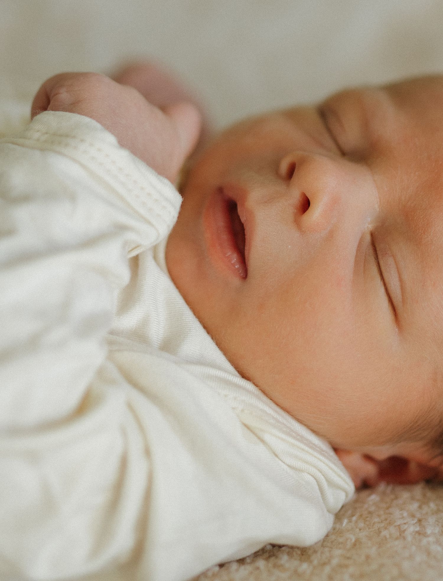 Peaceful sleeping newborn in white clothing on soft textured surface.