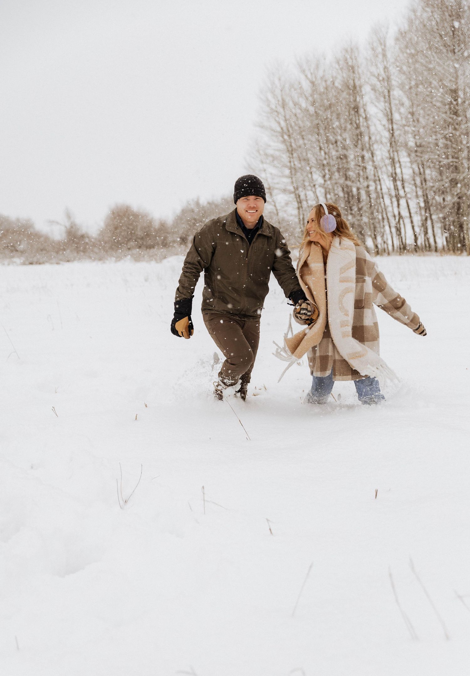 A couple walking hand in hand through deep snow in a winter landscape.