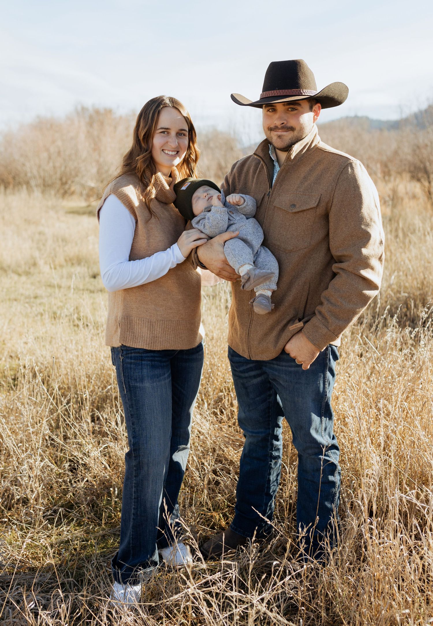 A western-styled family portrait in an autumn field with mountains visible in the background.