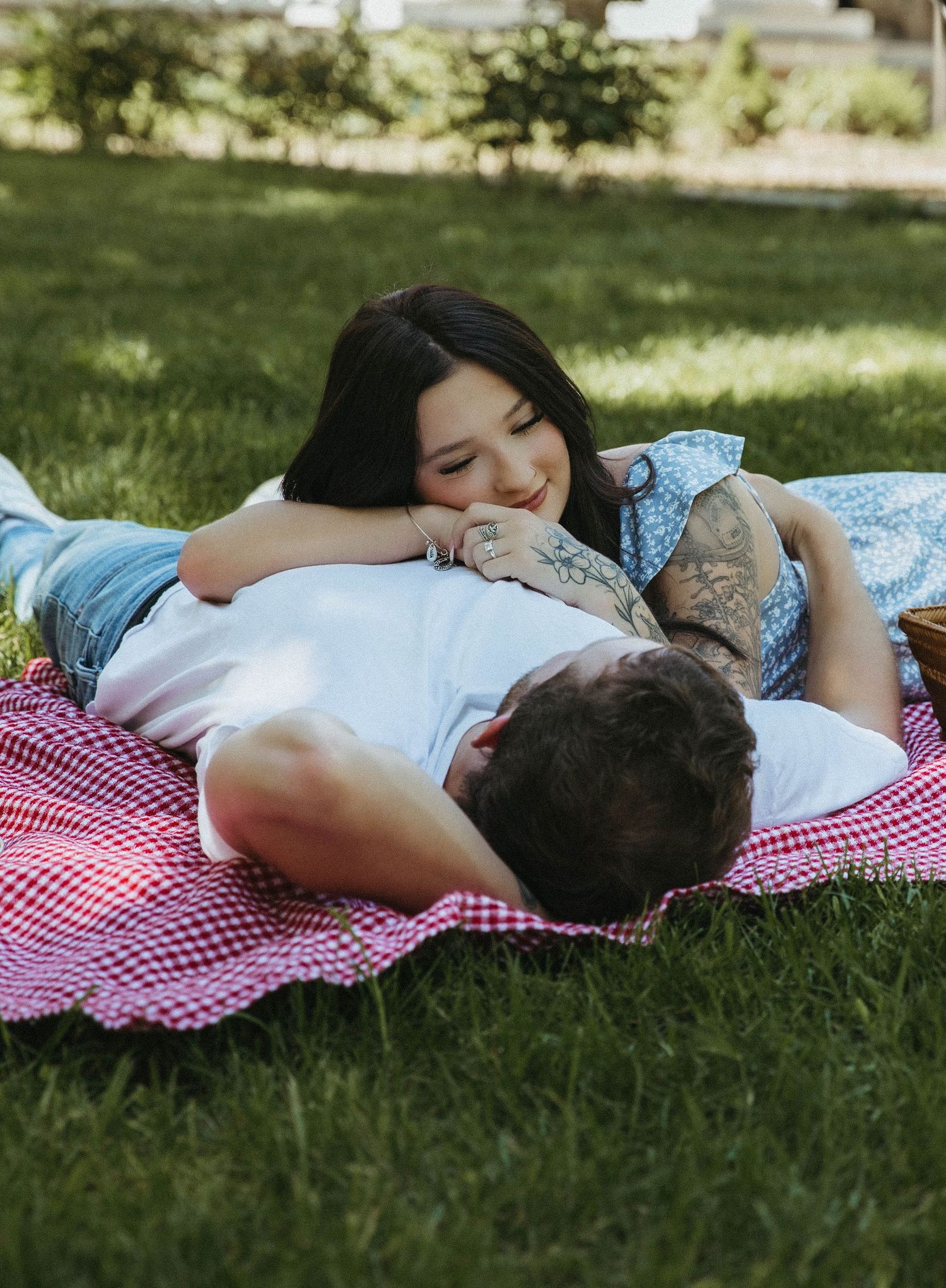 Person wearing a patterned shirt rests peacefully on a red and white checkered blanket in the grass on a sunny day.