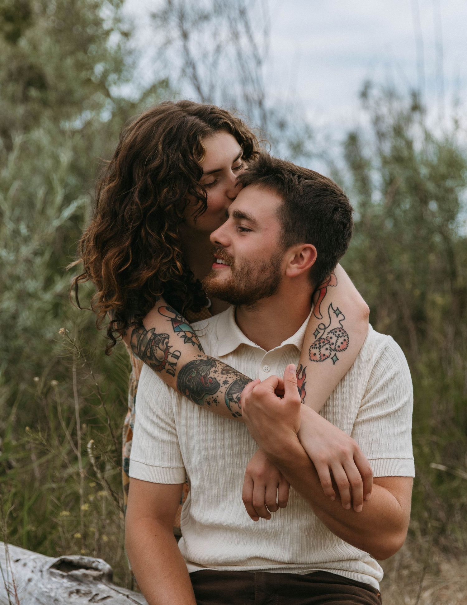 A romantic couple sharing intimate moments together in a grassy field on a cloudy day.