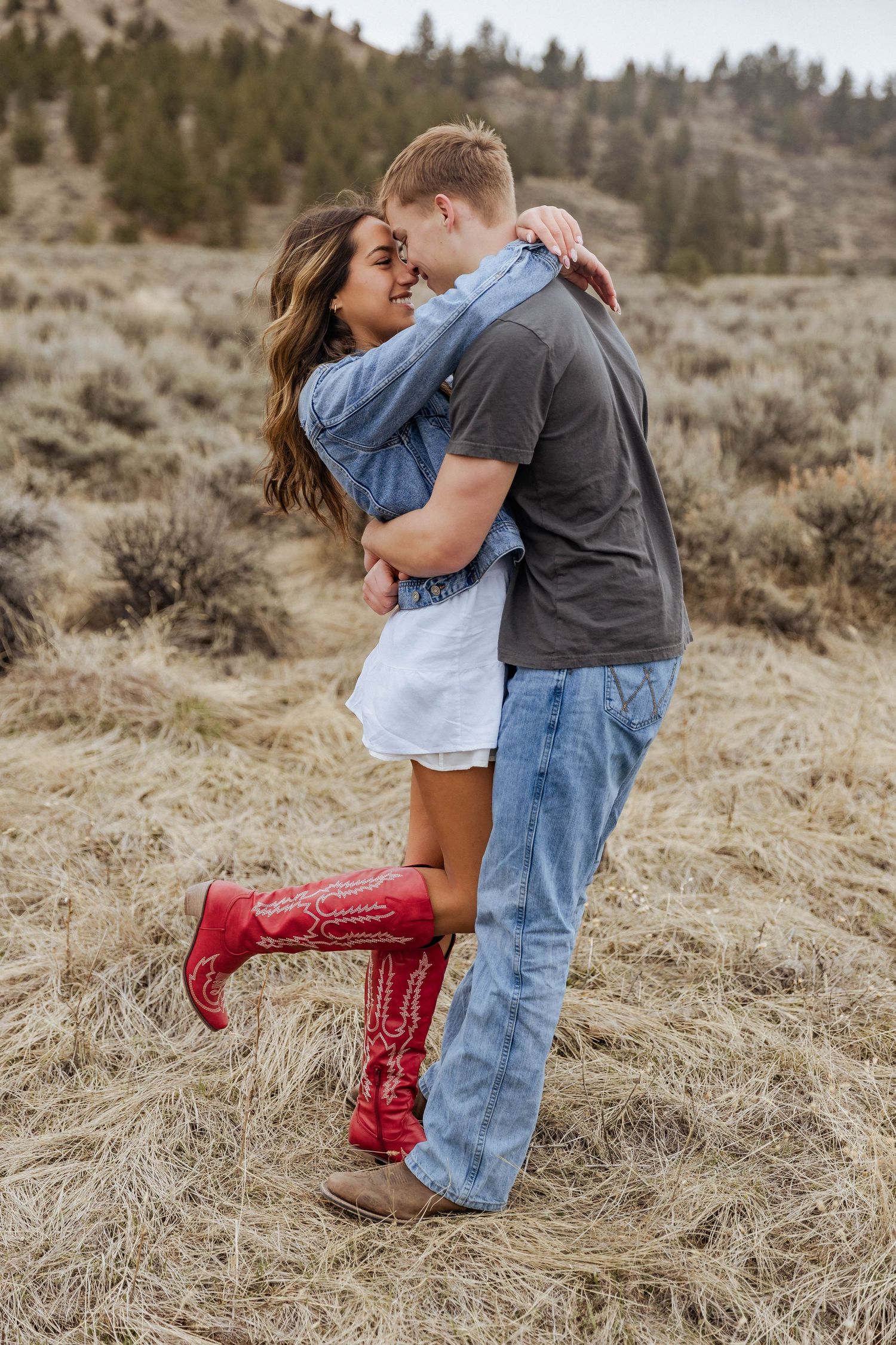 A romantic embrace in a rustic field with red boots adding a pop of color.