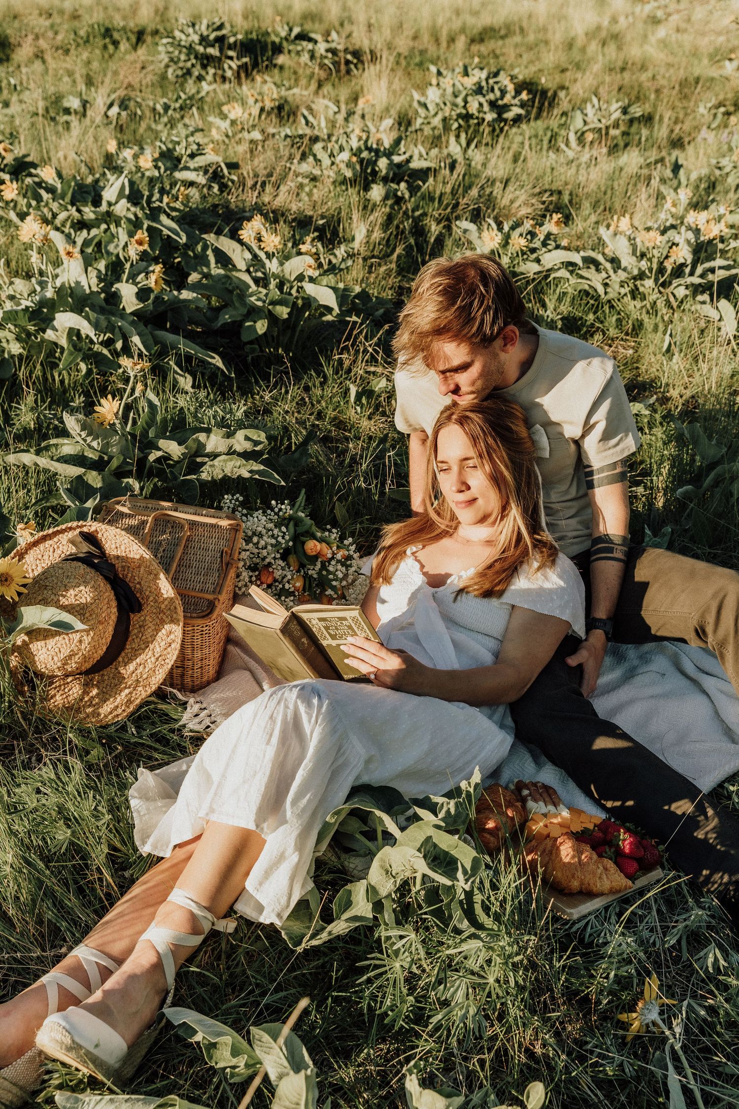 Couple relaxing in sunny meadow while reading together near picnic basket.