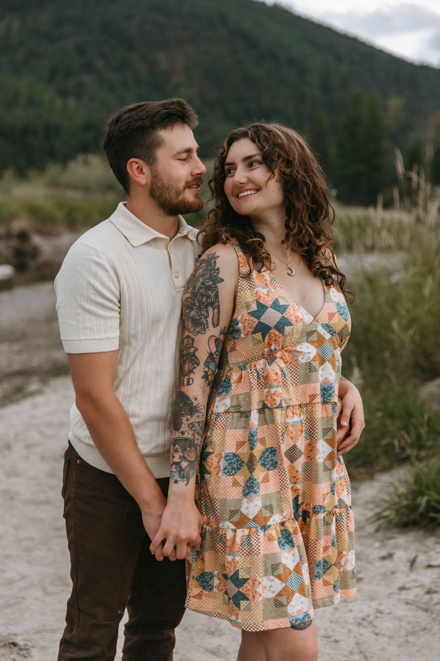 Happy couple shares intimate moments outdoors at sunset, wearing casual clothing and embracing by the mountains.