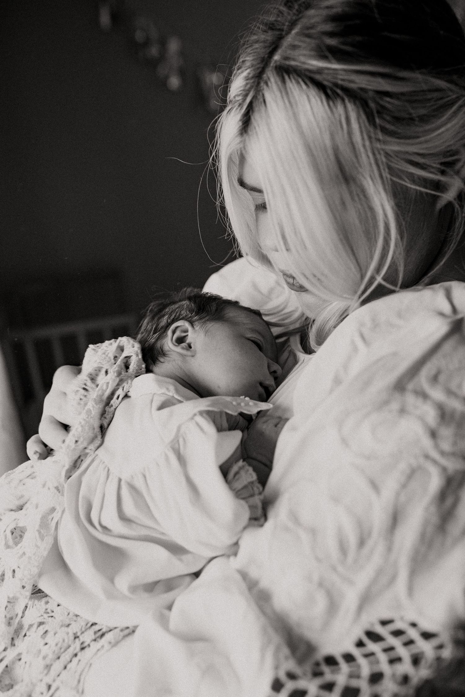 A mother gently kisses her babies forehead in the beautiful dim lit bedroom during their in home session