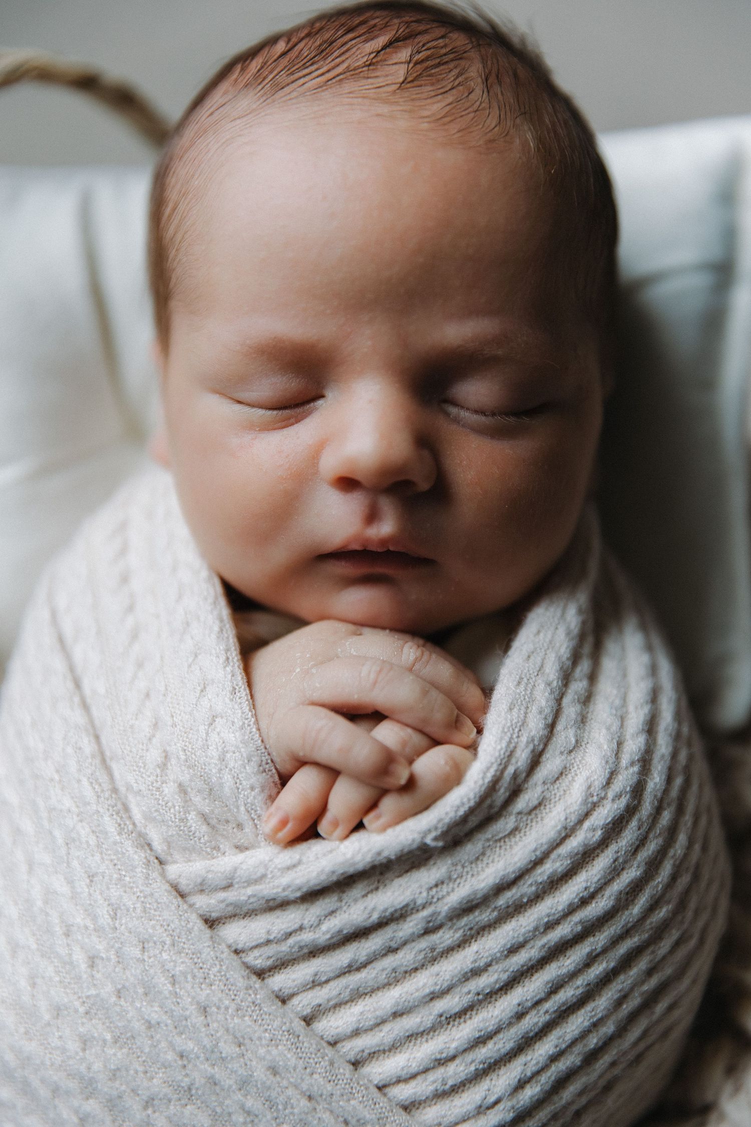 Sleeping newborn wrapped in soft white swaddle blanket with hands clasped together.