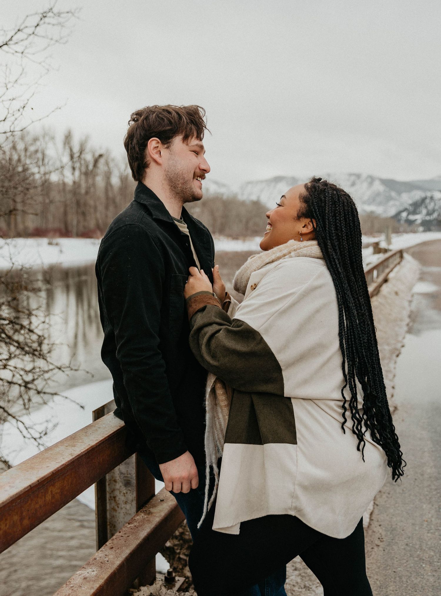 Couple sharing joyful moment on snowy mountain path with scenic winter backdrop.