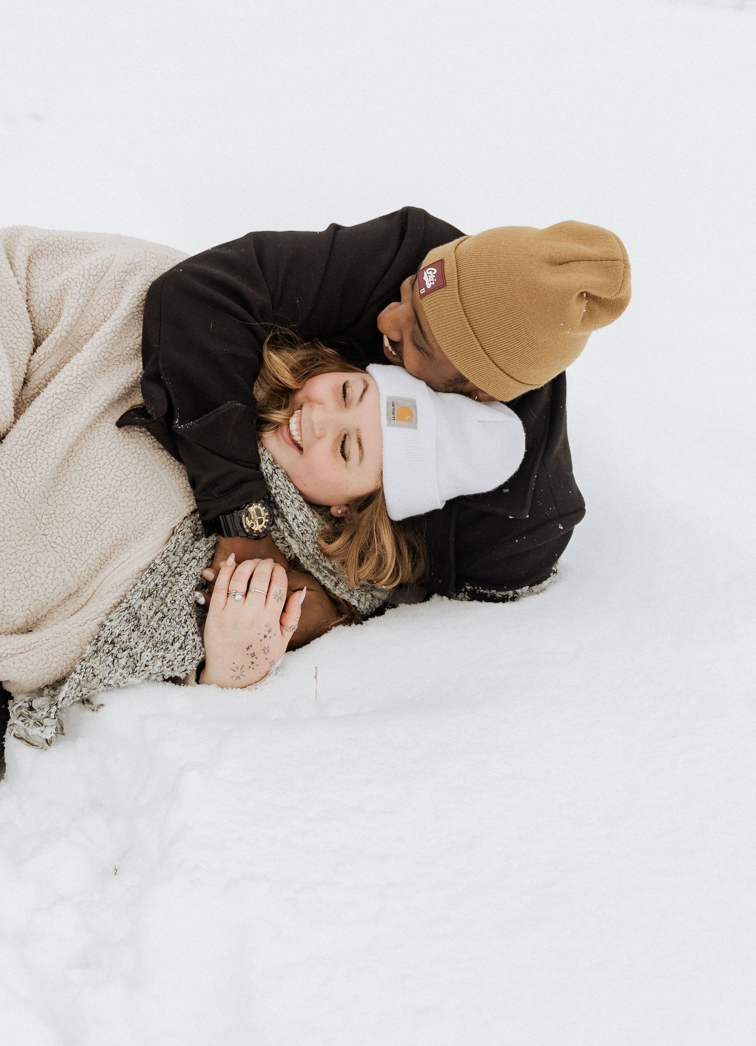A couple sharing a tender moment while lying in the snow together.