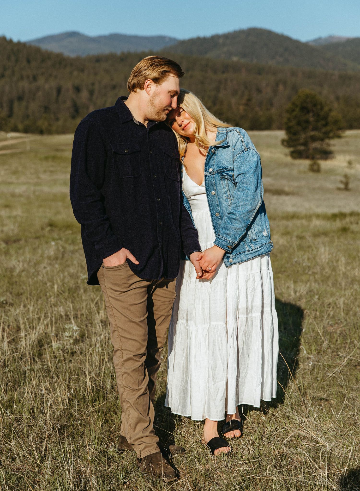 A couple shares an intimate moment in a golden field with mountains in the distance during sunset.