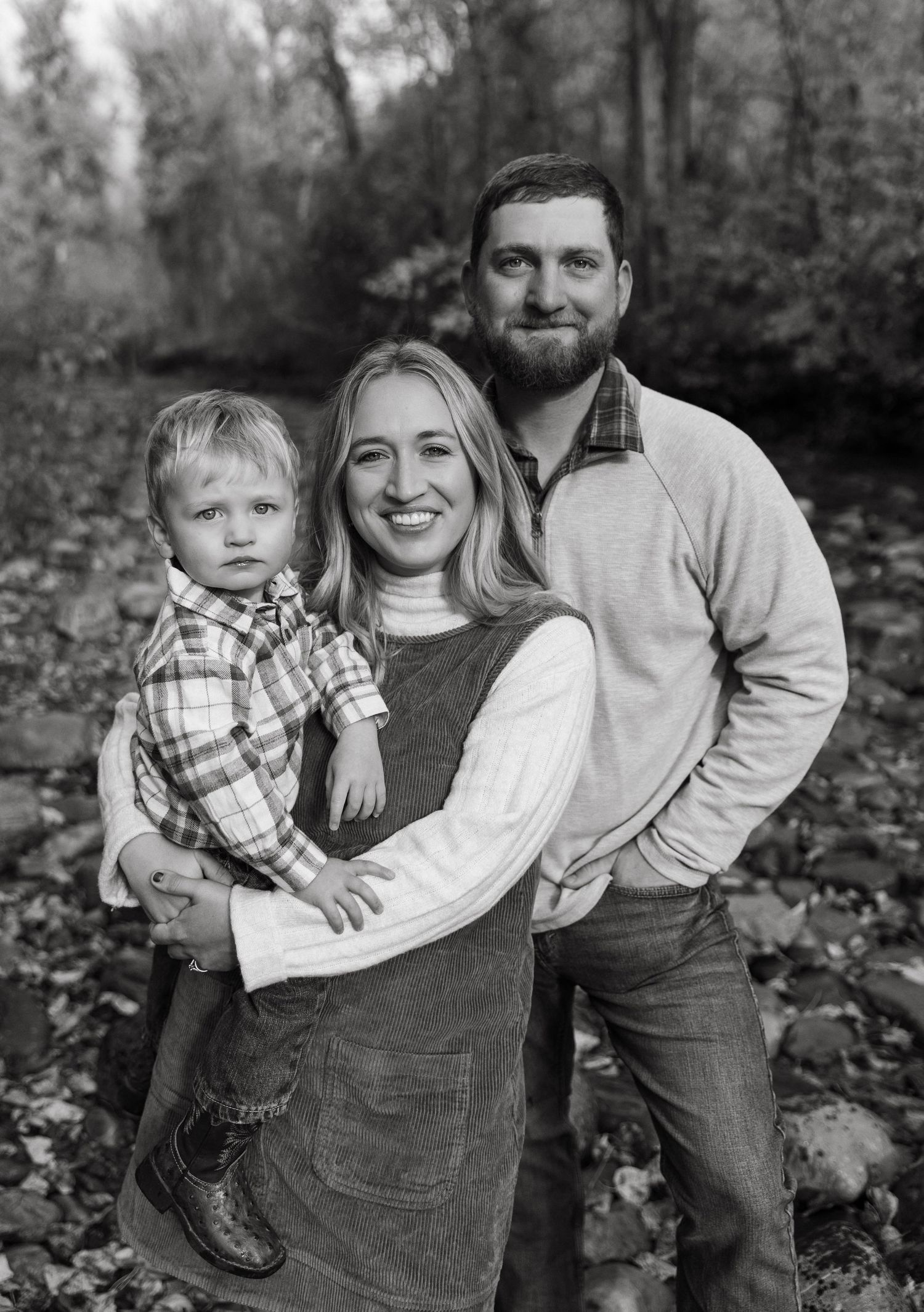 A black and white photo series showing a family of three posing together outdoors among fallen autumn leaves.