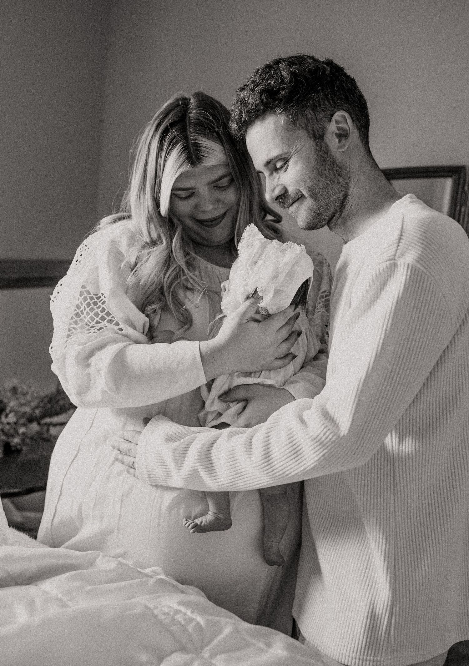 A black and white indoor portrait of new parents with their newborn baby.