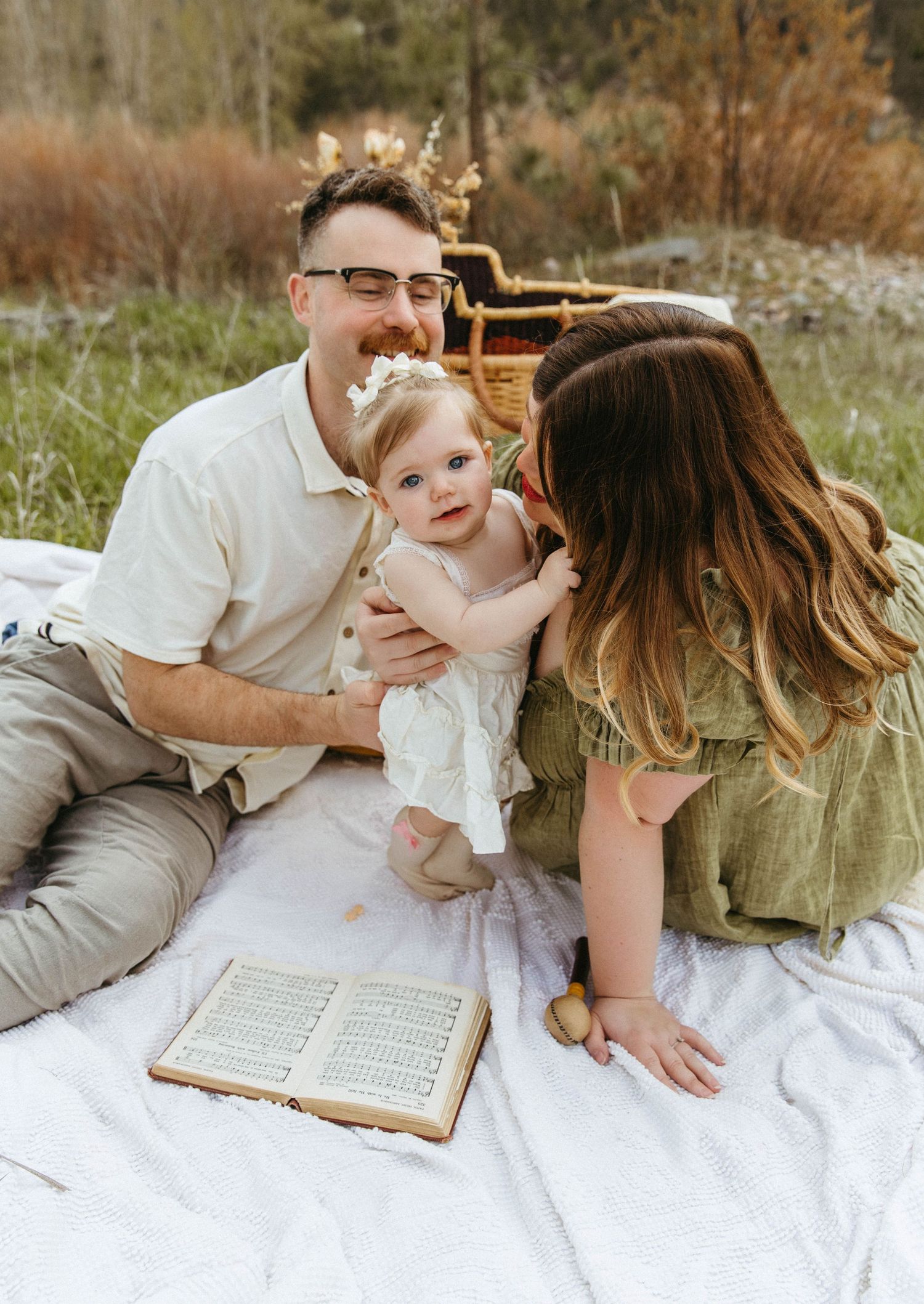 Sweet family moment captured during outdoor photoshoot on white blanket with antique book.