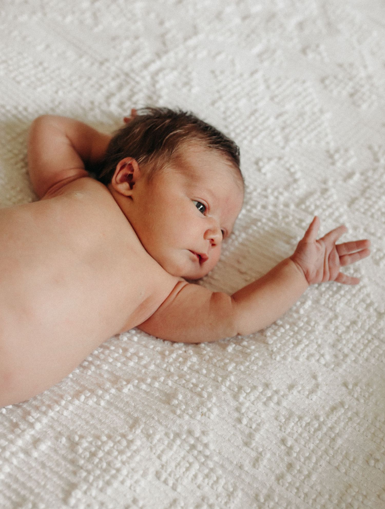 A newborn baby, laying on a visage blanket, stretches her arms.