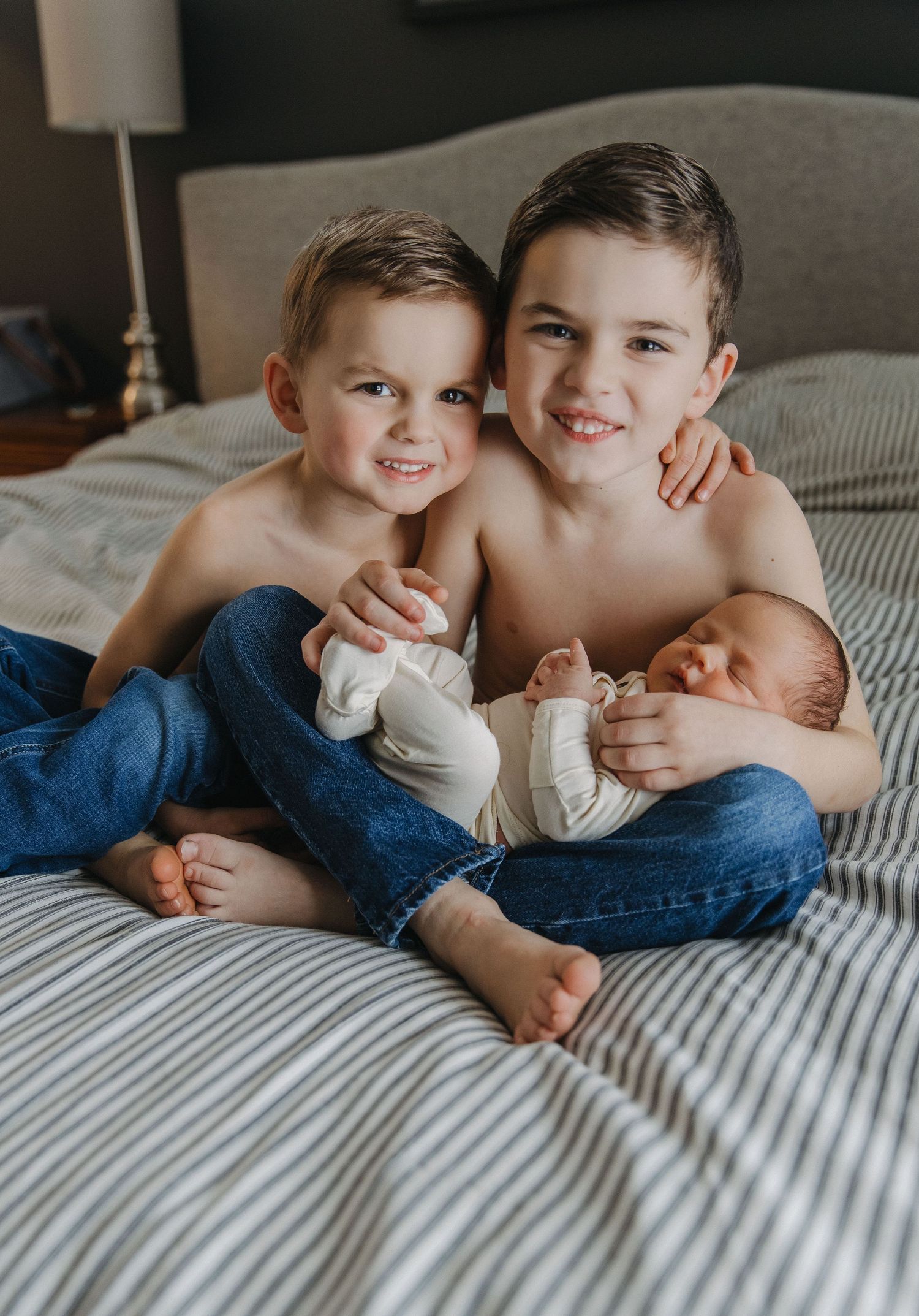 Three siblings sharing a sweet moment together on striped bedding.