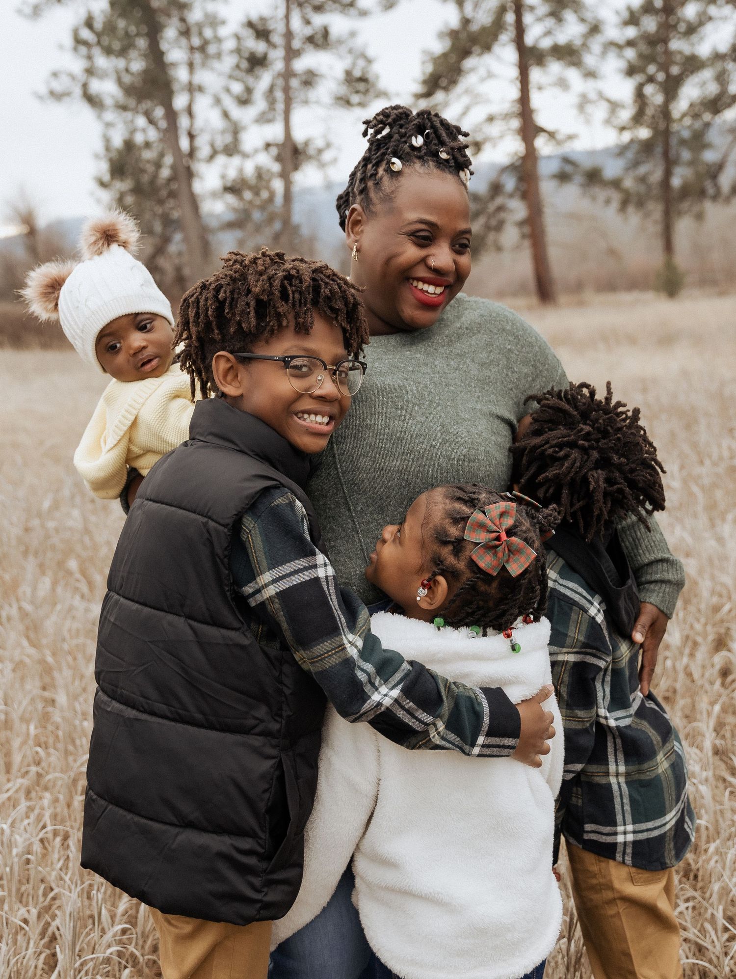 Happy family portrait in a field with tall grass and pine trees.