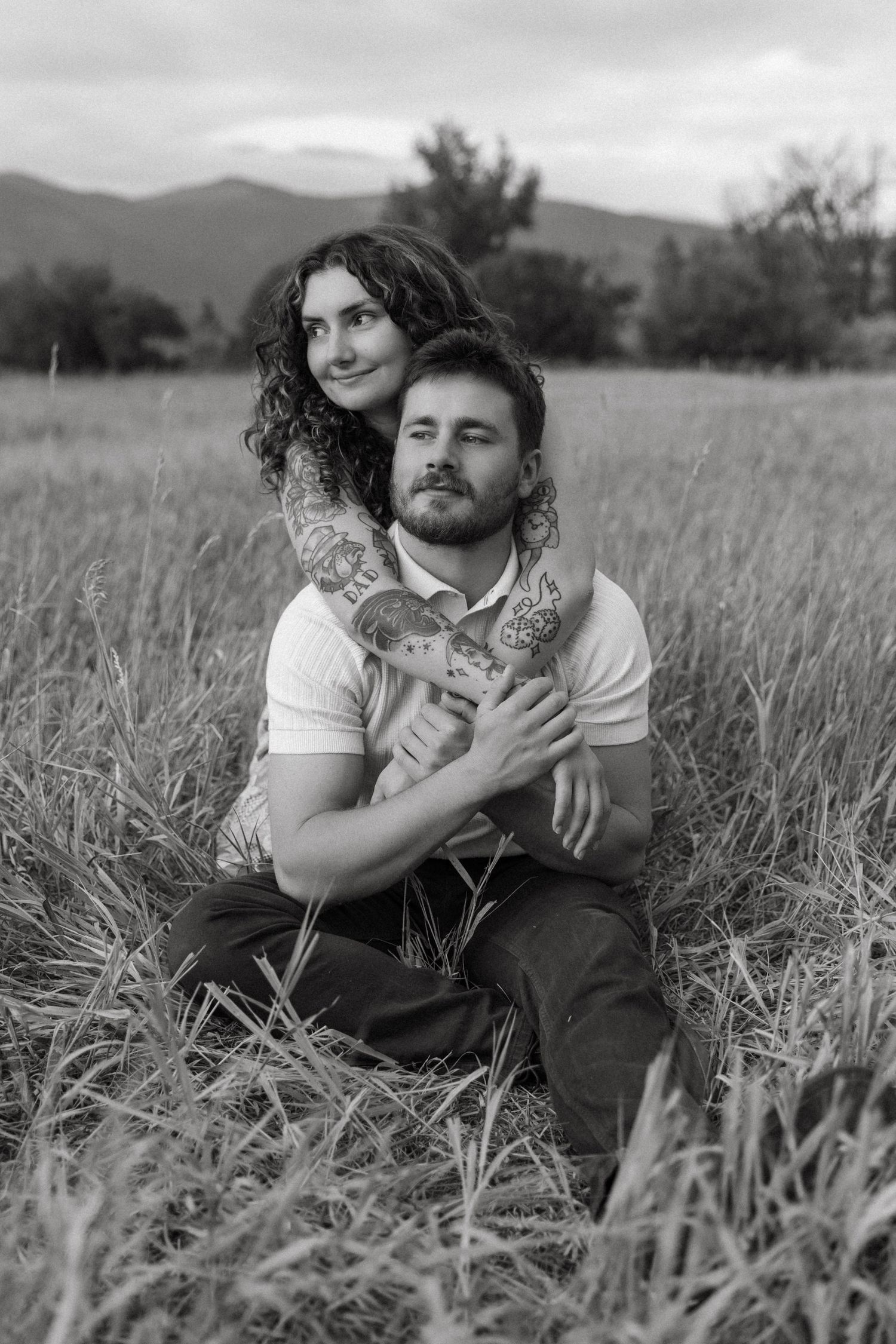 Monochromatic portrait series shows someone lying in tall grass holding a kitten in a tranquil outdoor setting.