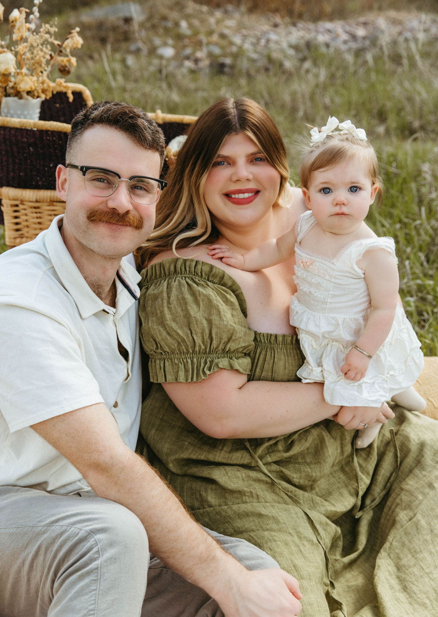 Family relaxing outdoors on a white blanket in a natural field setting with casual attire.