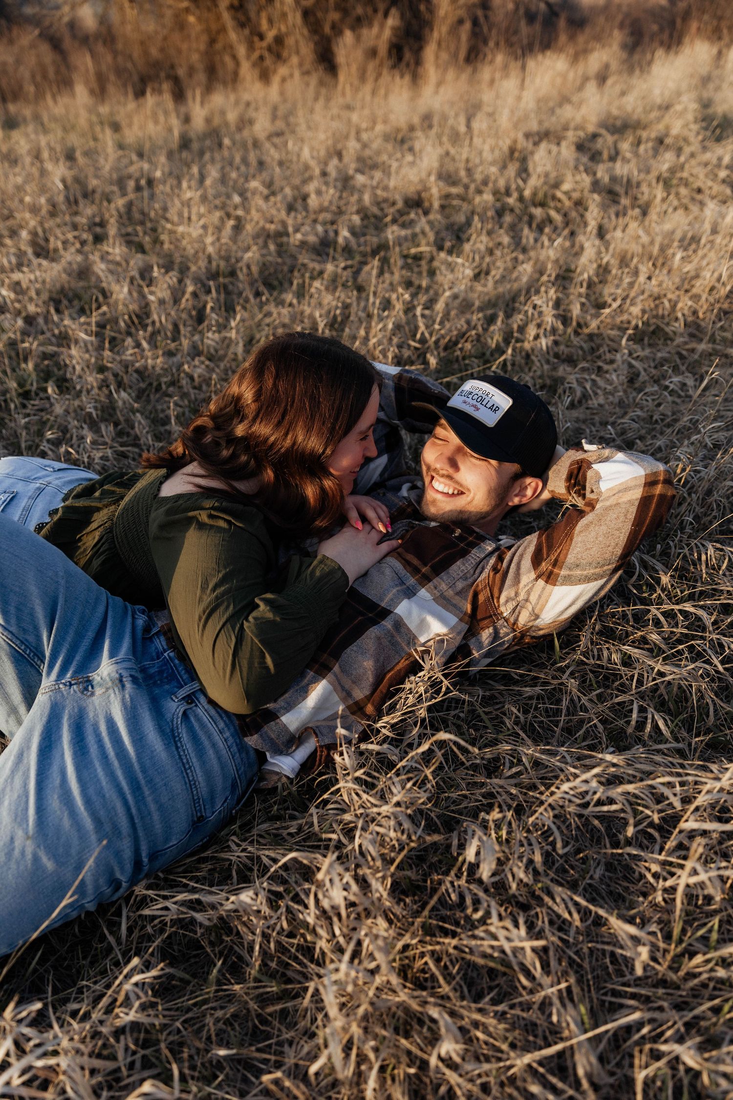 A couple laying in dry grass sharing a romantic moment during golden hour.