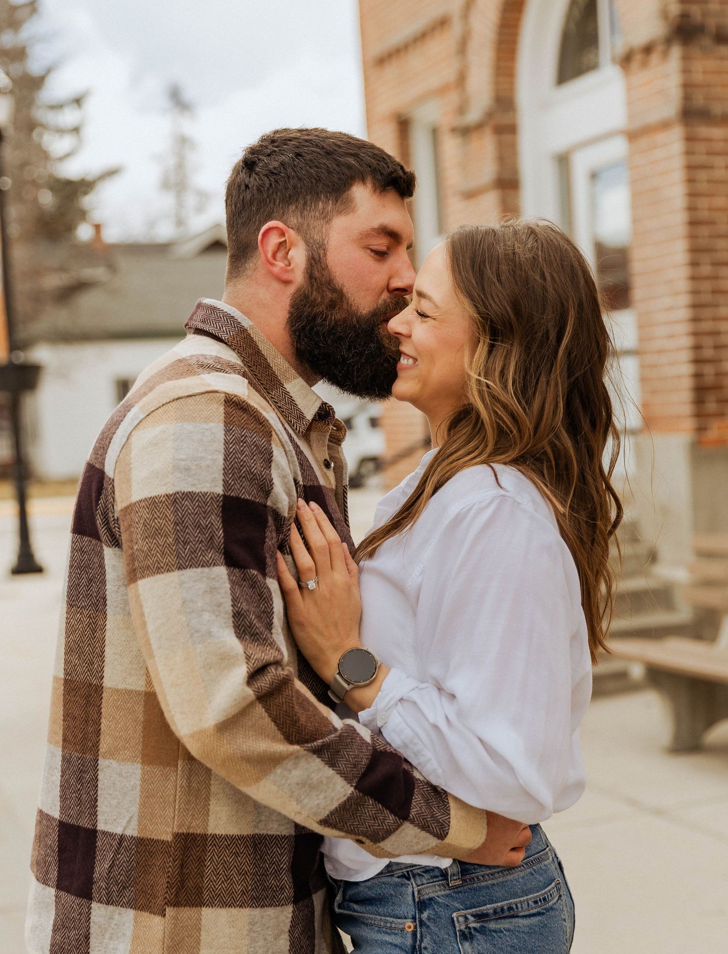 An intimate portrait of a couple sharing a close moment in front of a historic brick facade.