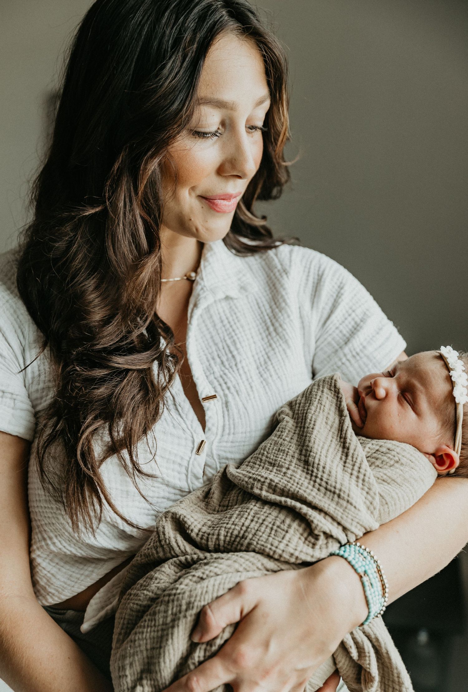 a mother stands in the window light holding her newborn baby, enjoying the moment