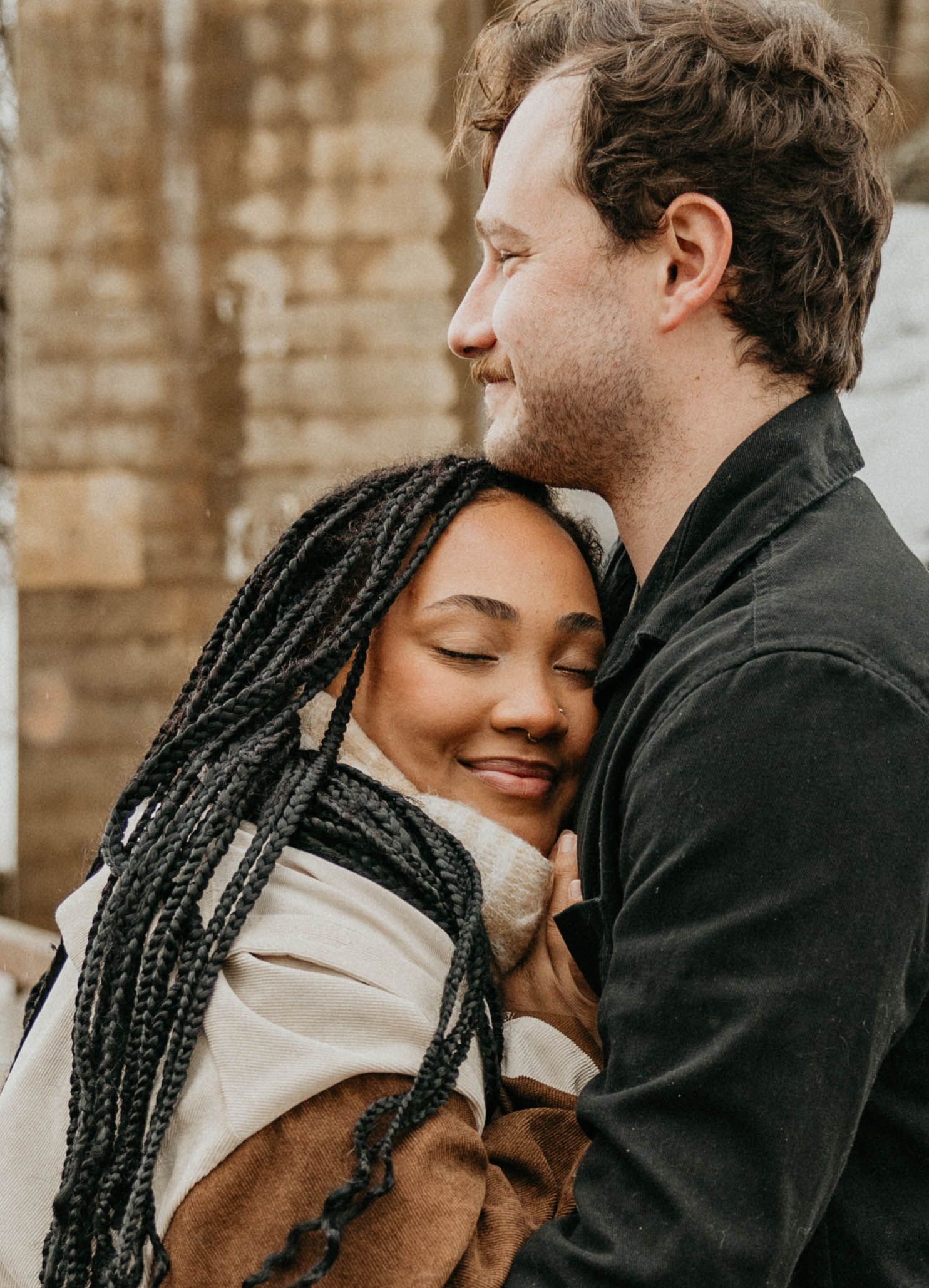 Intimate winter portrait of couple embracing against rustic backdrop.