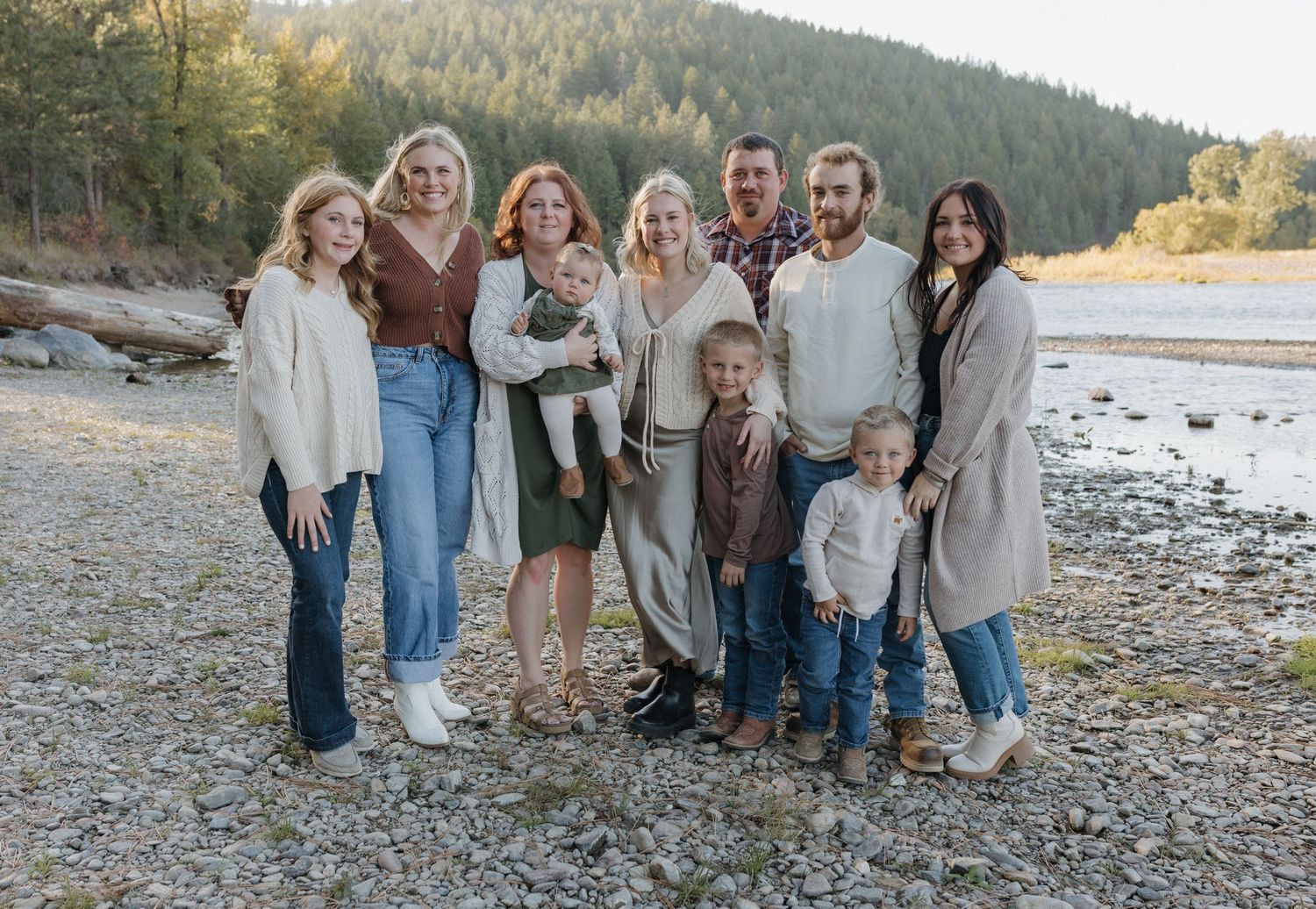 Extended family portrait on a rocky beach with mountains and forest in the background.
