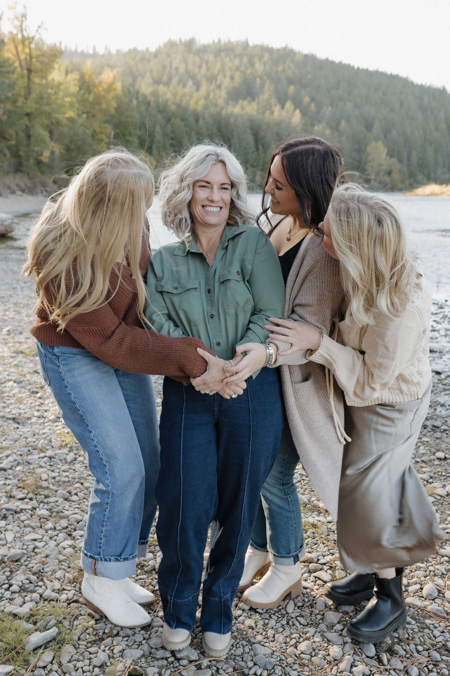 Women sharing joyful laughter while hugging in a circle on a rocky shoreline.