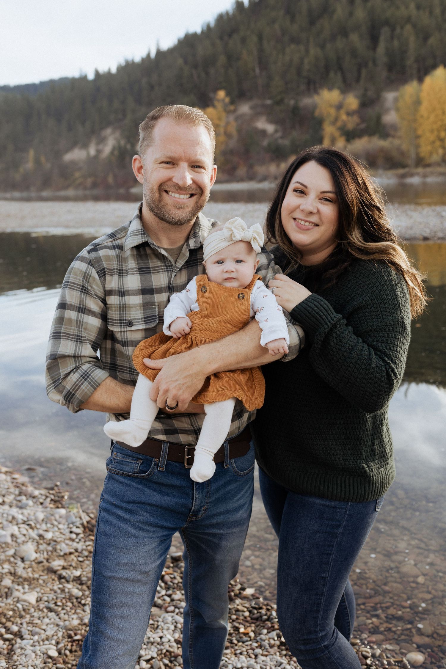 Family portrait by lake with mountain and autumn trees in background.