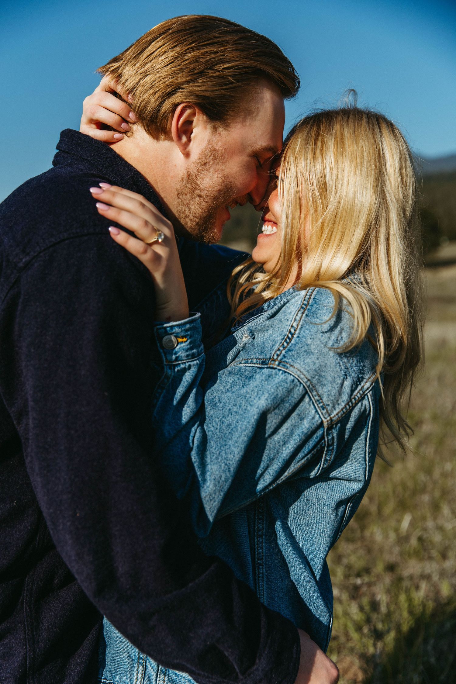 A romantic couple sharing an intimate moment outdoors in denim and dark clothing against a blurred nature background.