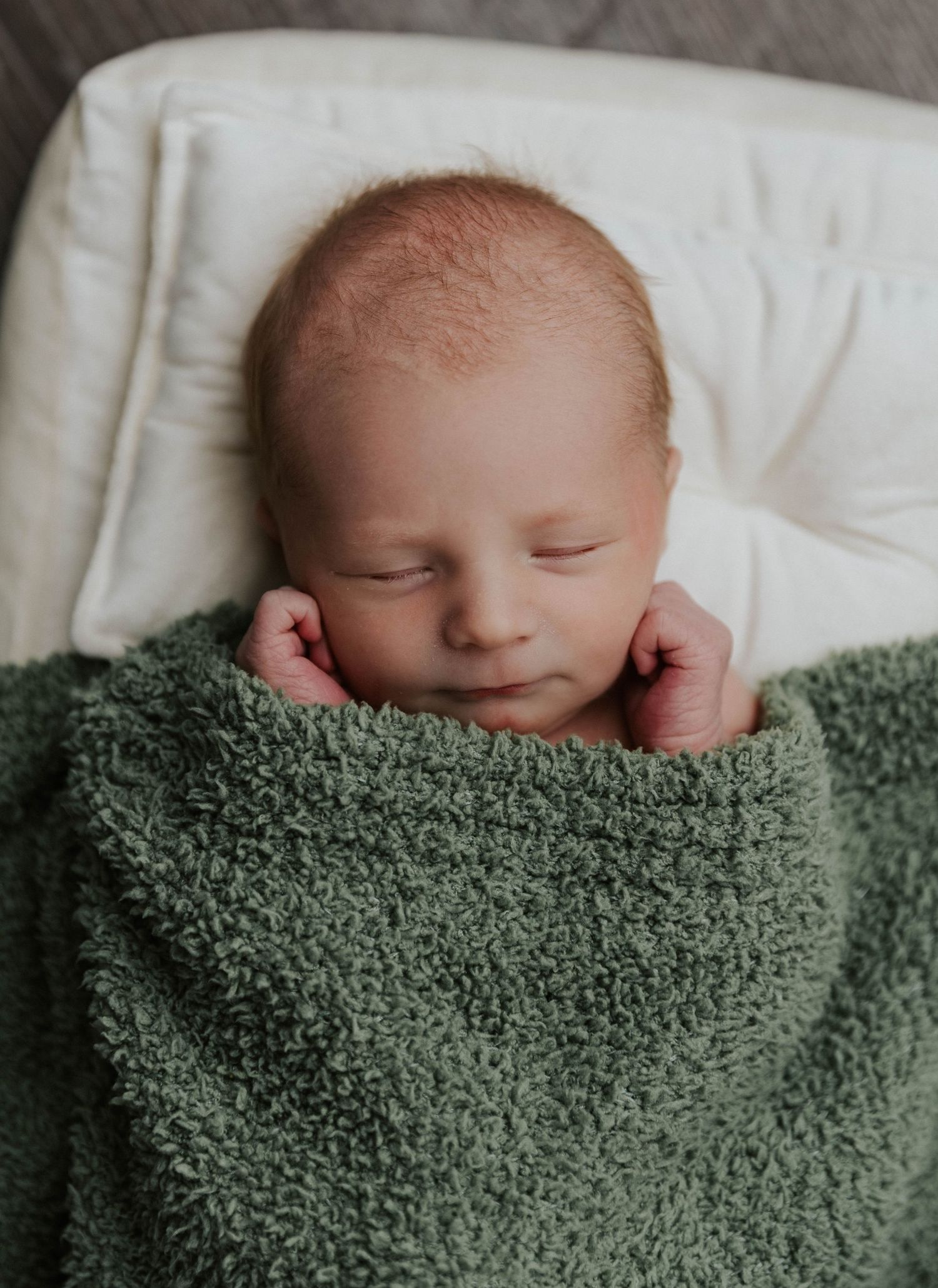 Newborn baby peacefully sleeping while swaddled in soft sage green blanket with textured knit pattern.