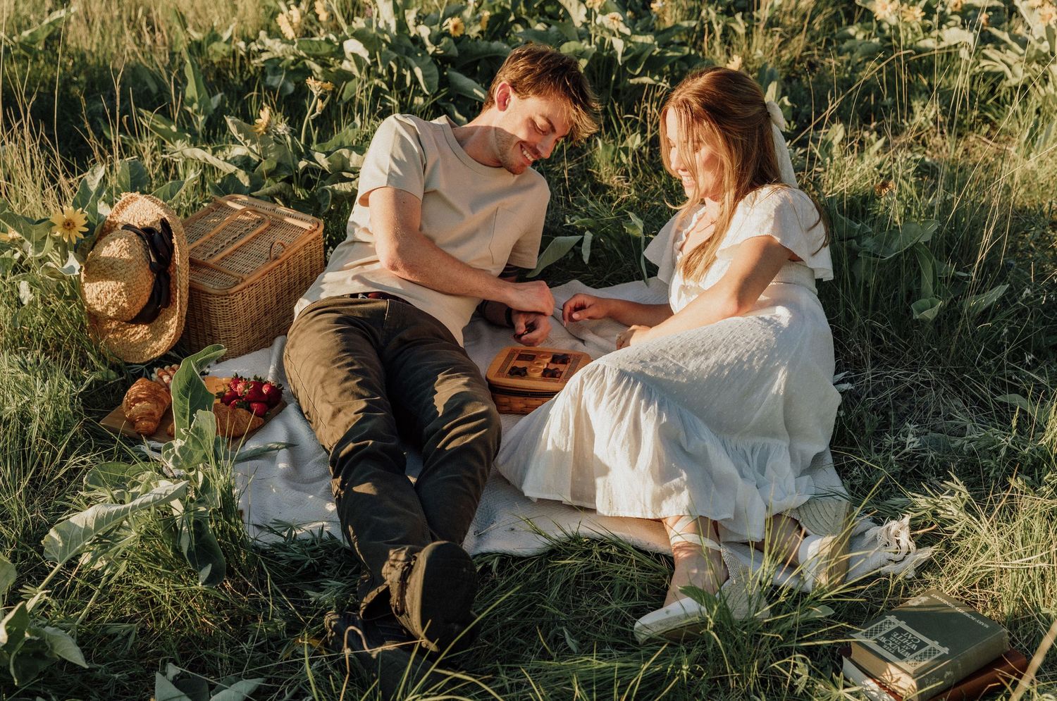 Couple having a sunny picnic on a blanket surrounded by wildflowers and a straw hat.