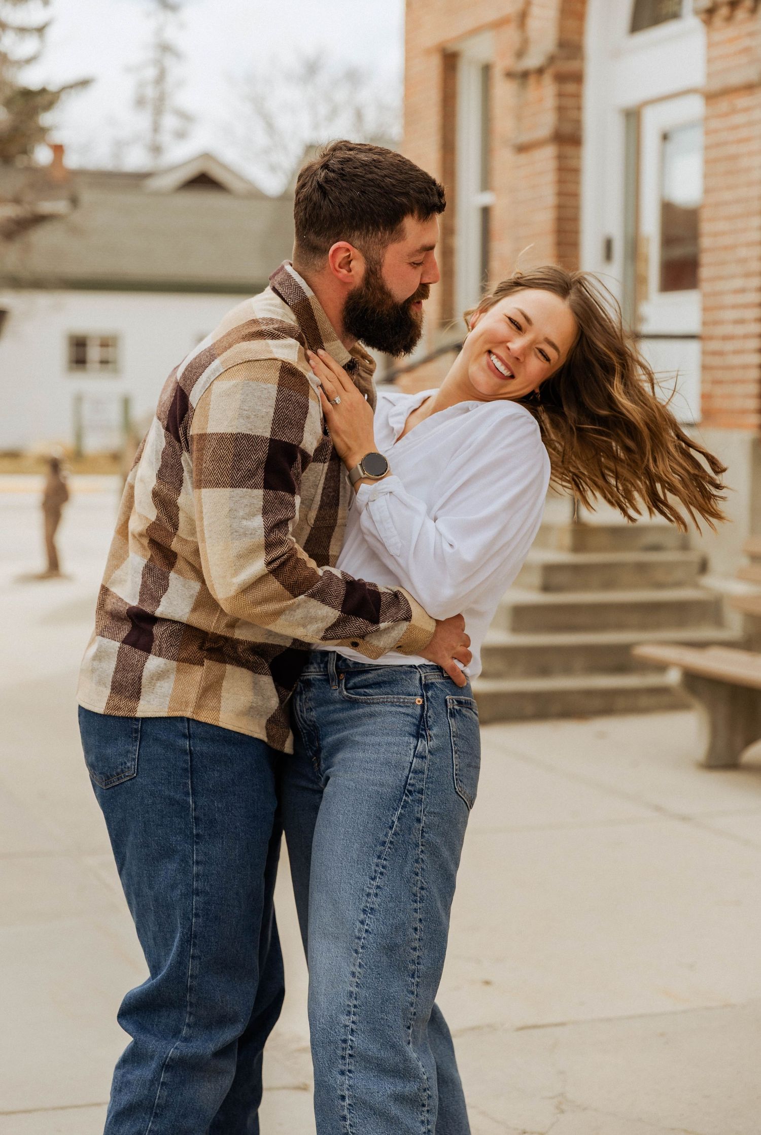A joyful couple laughing and dancing together outdoors near a brick building.
