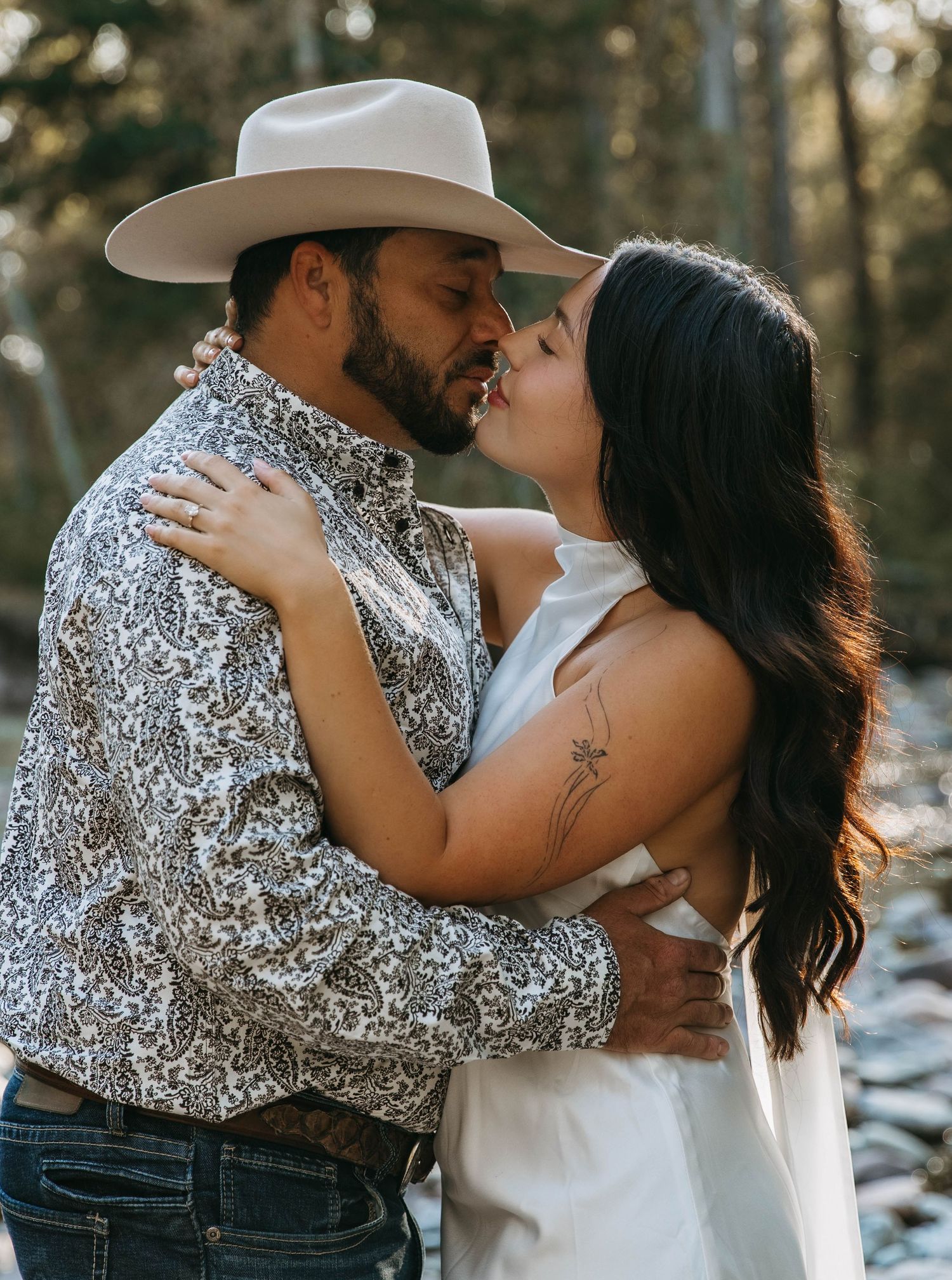 A romantic couple in western attire shares intimate moments in a snowy forest setting during a photo session.