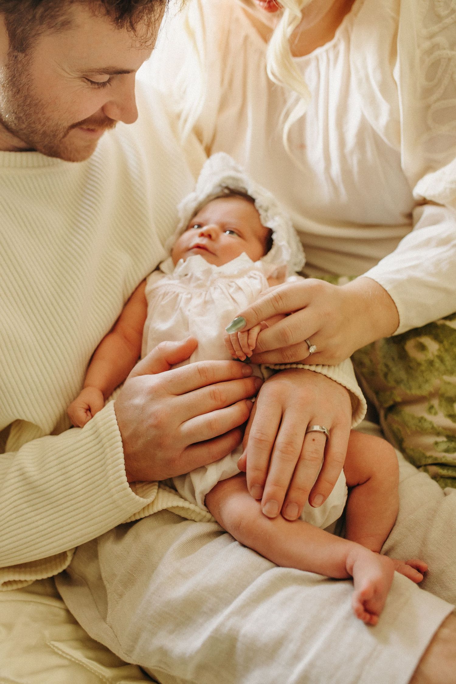 A tender moment between parents and baby showing wedding rings and white clothing.