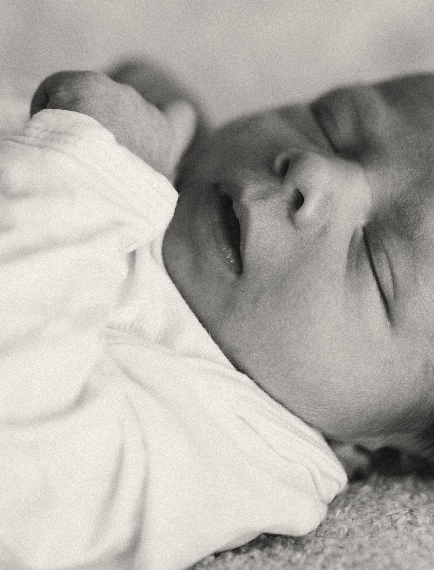 Close-up black and white portrait of sleeping infant in white clothing.