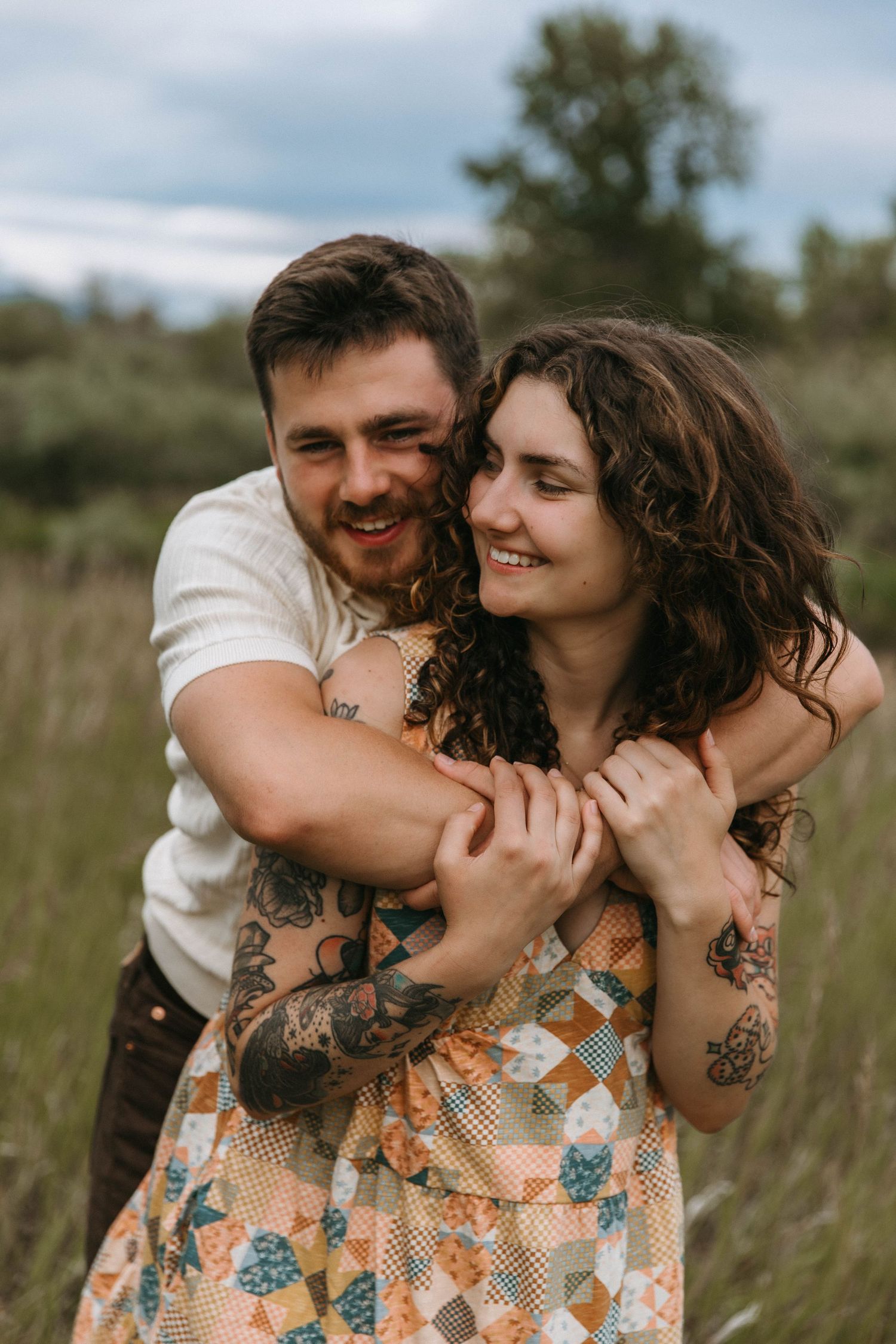 A couple shares intimate moments while embracing in a grassy field on an overcast day.