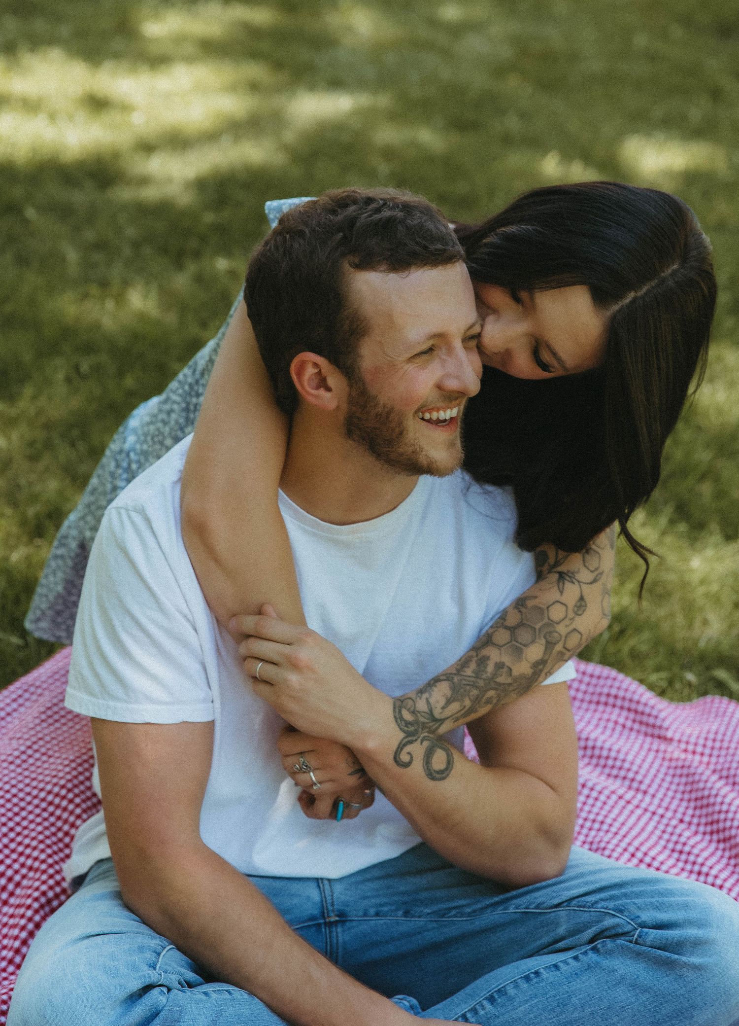 A couple shares intimate moments on a red and white checkered picnic blanket on a sunny day outdoors.