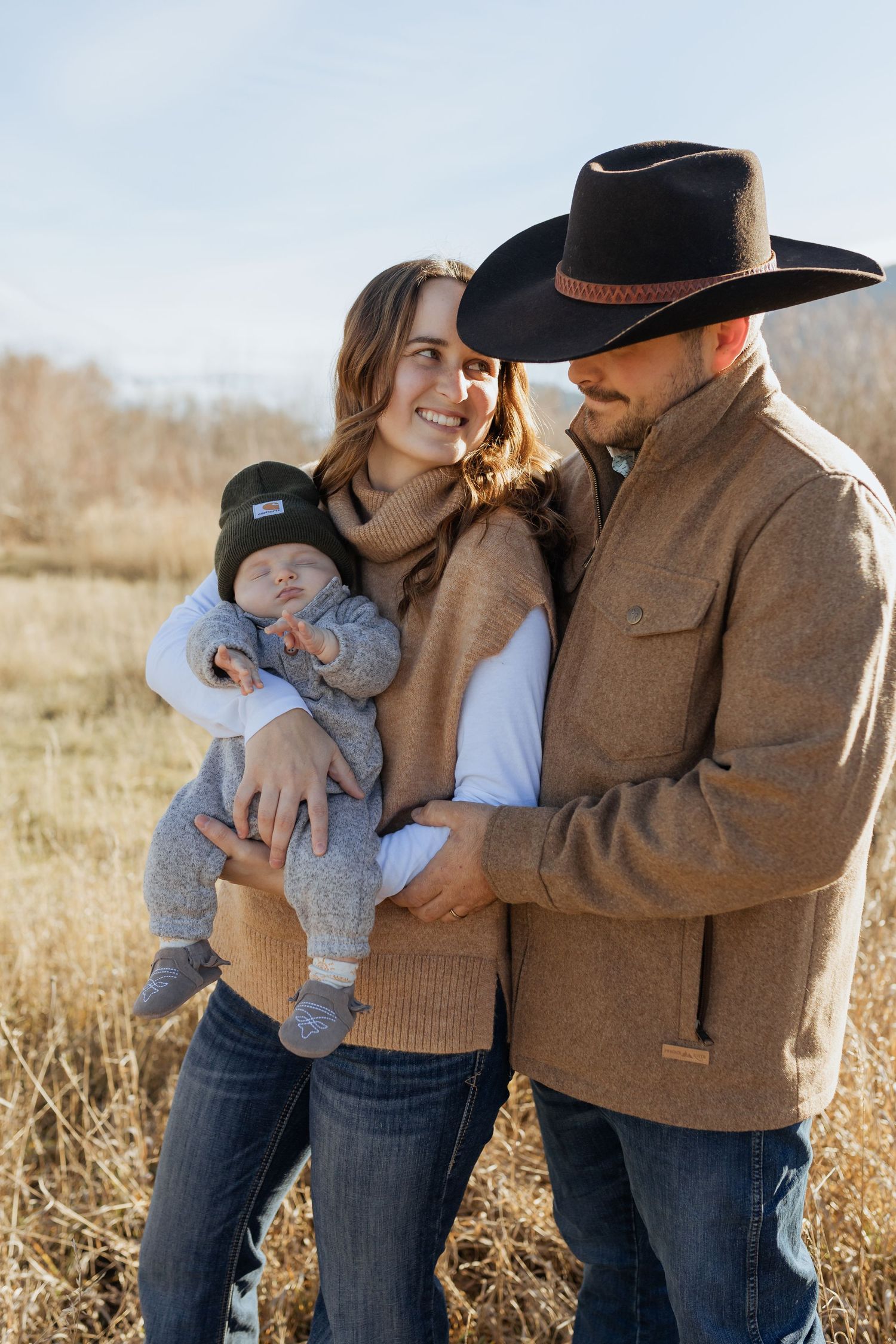 A family of three shares an intimate moment outdoors in brown autumn fields.
