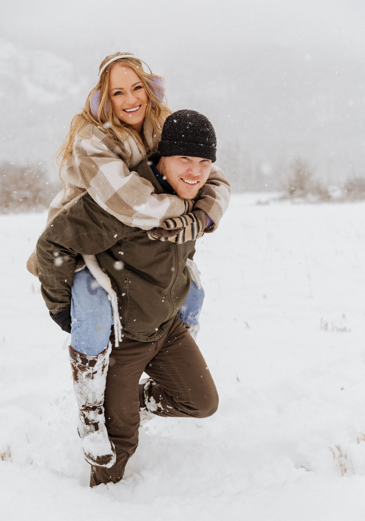 A joyful piggyback ride in the snow with a couple wearing winter clothing.
