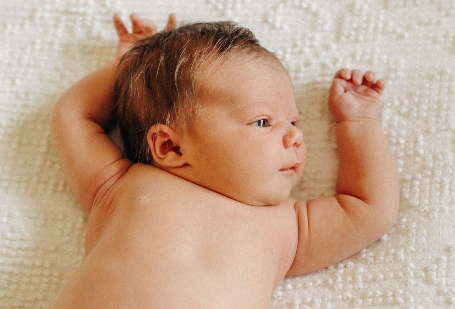 A newborn baby, laying on a visage blanket, stretches her arms.