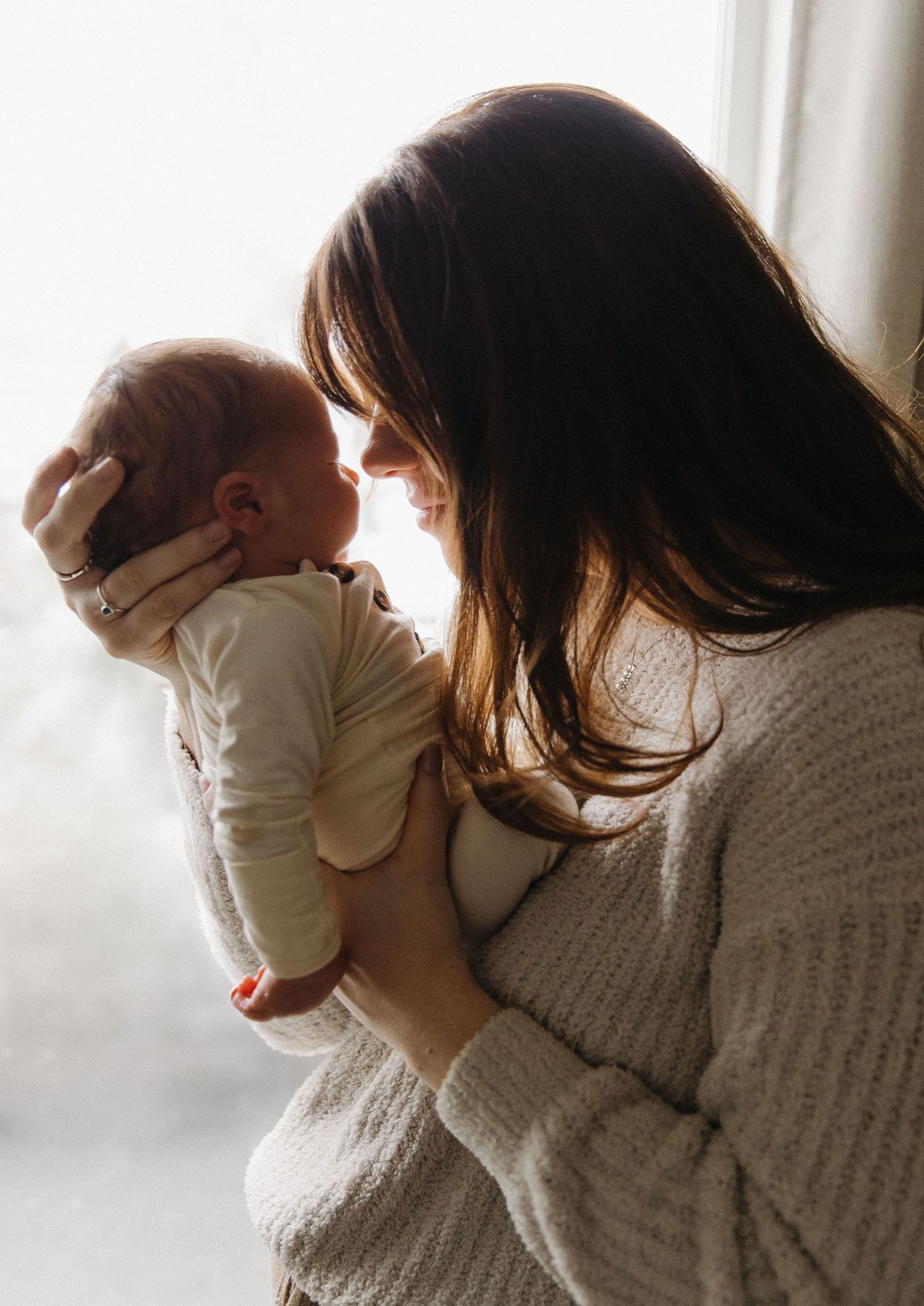 Intimate moment between parent and infant by window in natural light.