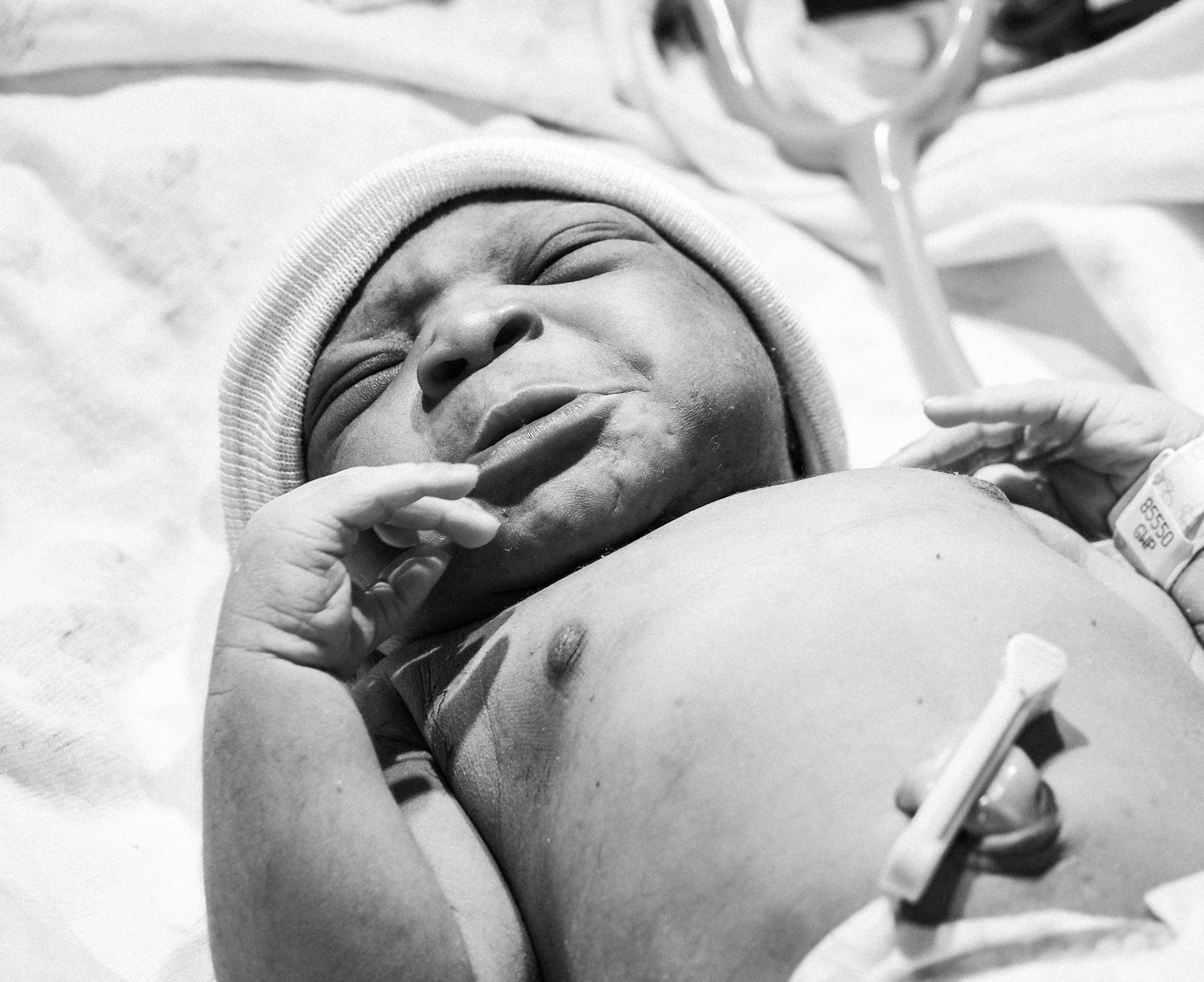 Detailed black and white profile shot of a newborn baby's face against white bedding.