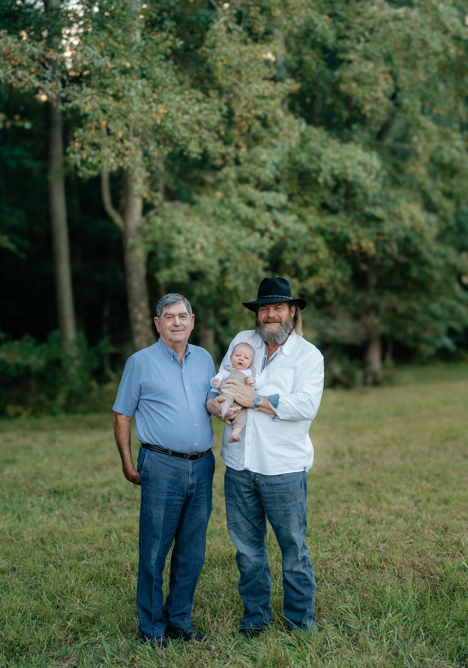 Three people standing together in casual attire on grassy field.