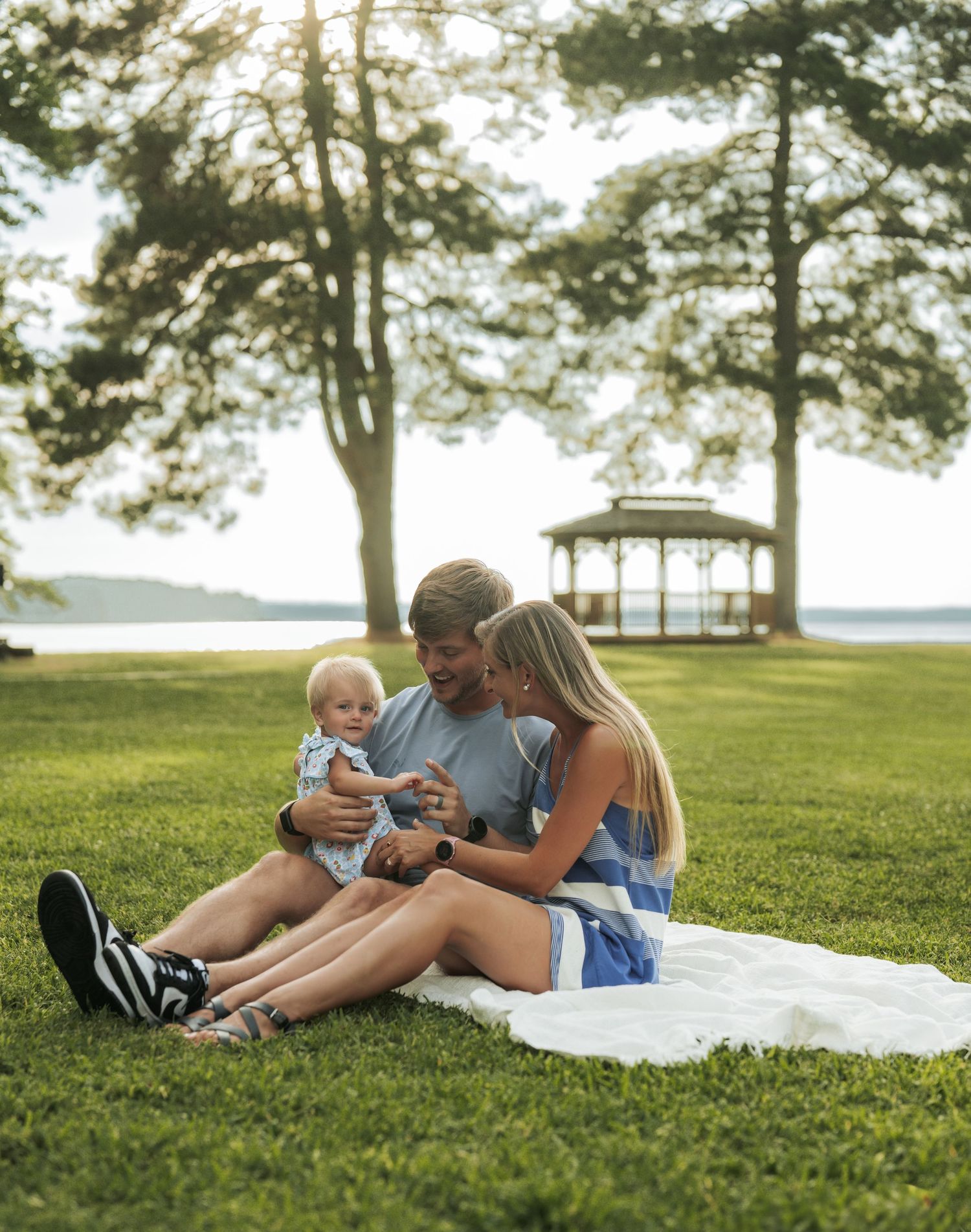 Family relaxing together on white blanket in grassy park during summer evening.